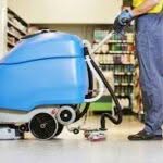 addetto delle pulizie delle quali si vedono solo braccia e gambe che trasporta un grosso macchinario celeste per il trattamento di un pavimento