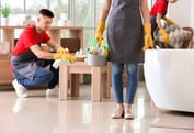 3 addetti alle pulizie stanno lavorando in un appartamento tutti con camice e divisa maglia rossa e pantalone blu con guanti due uomini e una donna