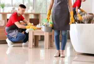 3 addetti alle pulizie stanno lavorando in un appartamento tutti con camice e divisa maglia rossa e pantalone blu con guanti due uomini e una donna
